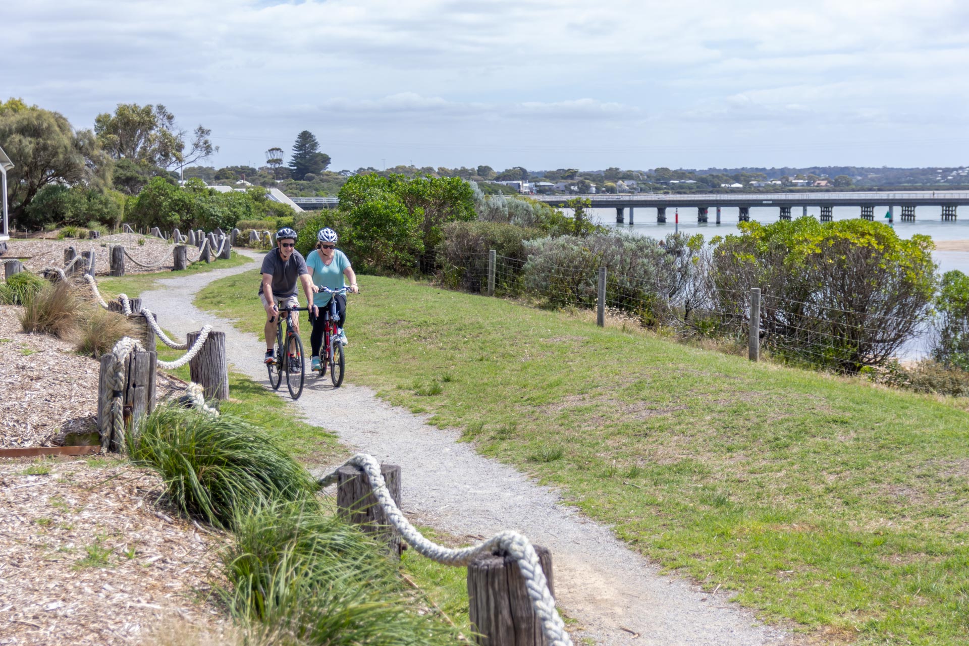 A couple riding a bike along the path with a view of the Barwon Heads Bridge