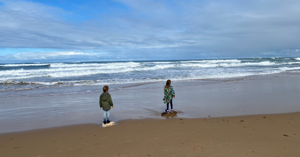 Two kids standing on the beach looking out to sea